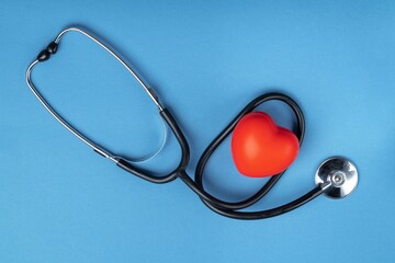 Stethoscope and rubber red heart on a blue background with space for text. Heart health, healthcare concept. Flat lay