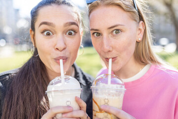 Surprised female friends drinking milkshakes at park