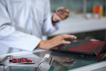 Fototapeta premium Young Asian male pharmacist checking drugs in pharmacy inventory using a computer at a pharmacy high quality photos