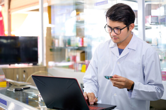 Young Asian male pharmacist checking drugs in pharmacy inventory using a computer at a pharmacy high quality photos