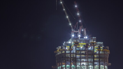 High multi-storey building under construction and cranes at night timelapse