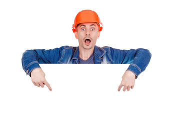 Young working man in orange hard hat with a happy face, isolated on white background. Cheerful male industrial engineer in uniform. Builder points to empty space for ad text. Safety equipment.