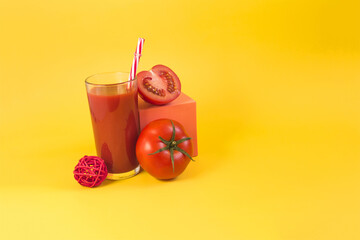 Natural tomato juice in a glass container with a decor of tomatoes, salt and a colored cube on a bright yellow background