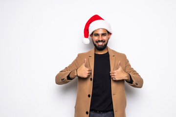 Young handsome man in business suit and Santa hats on white background in studio smilie and showing thumbs up