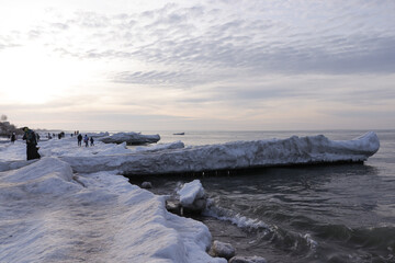 Winter Baltic Sea in Zelenogradsk Kaliningrad region. The sea is frozen over, there are many snow blocks. Seagulls fly over the icy breakwaters. People walk on the frozen sea.