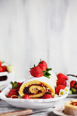 Homemade strawberry shortcake cake roll or Roulade with a berry jam filling and powdered sugar. Dessert over a white rustic wooden table. Selective focus with blurred foreground and background.