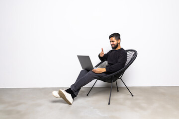 Young man freelancer is at home, sits in a chair and communicates online. A young man on a laptop eran uses a video call and video chat. Working online, remote communication.