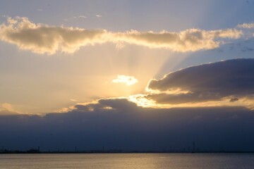 Naklejka na ściany i meble 兵庫県芦屋市芦屋浜の夜明け。雲に覆われていて太陽が雲の間から顔を出し、天使の梯子が海に落ちる