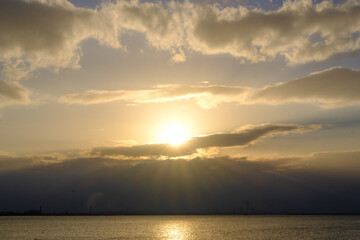 兵庫県芦屋市芦屋浜の夜明け。雲に覆われていて太陽が雲の間から顔を出し、天使の梯子が海に落ちる