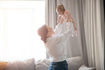 Portrait of young mother and newborn baby in her arms at home, morning exercises for healthy growth of infant, sunlight