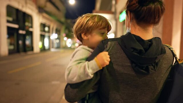 Mother carrying toddler child in arms walking at night in street