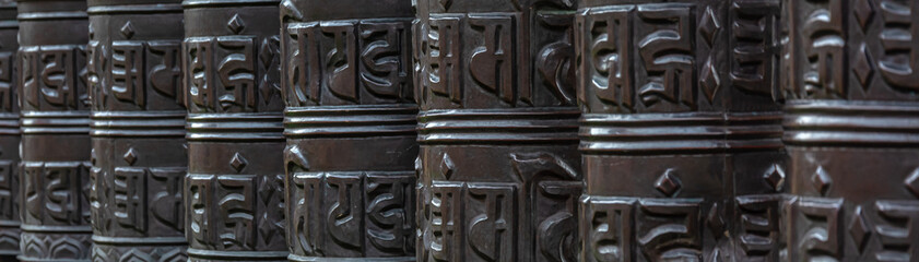 Background image of Tibetan Buddhist prayer drums arranged in a row. Blurring drums in the background