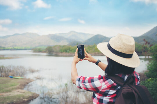 woman stand on the banks of the lake using her cell phone send message sms e-mail, taking pictures, Video call, Asian woman hiker in front smiling happy, Woman hiking in woods, warm summer day.