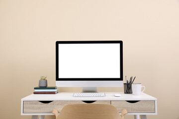 Comfortable workplace with blank computer display on desk near beige wall. Space for text