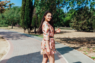 beautiful brunette woman in a dress with flowers walks along the street and the park