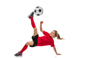 Full-length portrait of girl, child in red uniform training football isolated over white background