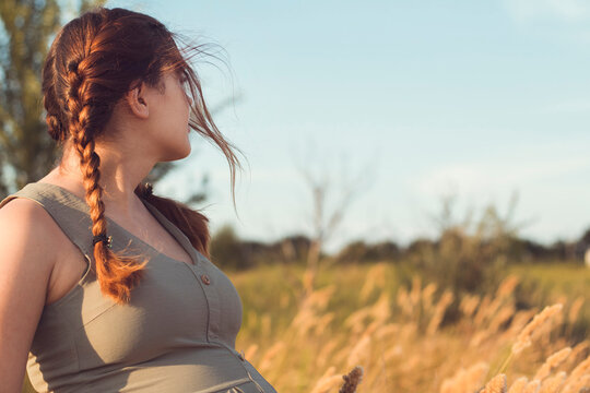 young beautiful pregnant woman looking ahead in field, relaxation on summer nature, preparation for childbirth, happy healthy motherhood