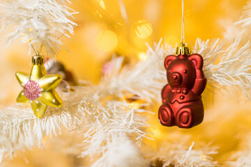 Close up of red bear toy and garlands on white yellow Christmas tree