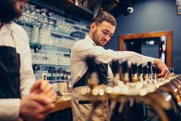 Two handsome bartenders poring beer at pub