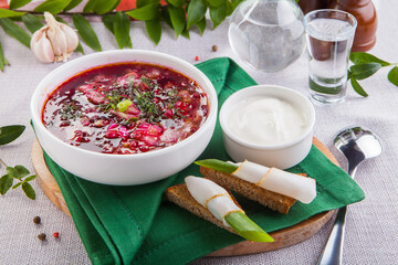 Borscht in a white plate. Next to it is sour cream and croutons with lard.