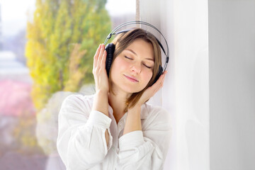 Happy girl wearing headphones. Relaxed young woman enjoying calm music in wireless earphones at home