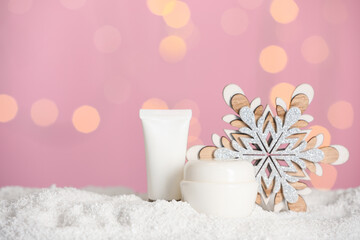 Obraz na płótnie Canvas Set of winter skin care cosmetics with hand cream and decorative snowflake on snow against blurred lights. Space for text