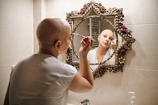 Mature woman with cancer brushing eyebrow while looking at reflection in mirror