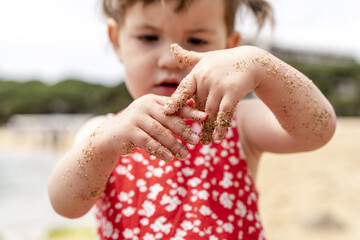 Girl looking at dirty hands while standing on beach