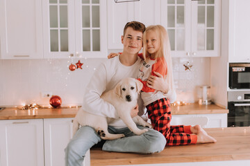 children with their beloved dog are sitting in the Christmas kitchen. family pastime. lifestyle. brother and sister, boy and girl play and fool around with a pet. space for text. High quality photo