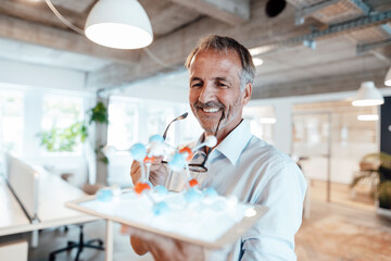 Smiling businessman holding digital tablet and artificial molecule in office