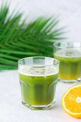 Cold matcha cocktail with orange juice on the background of a palm branch.