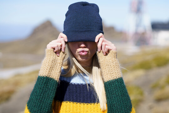 Young woman puckering while covering eyes with knit hat