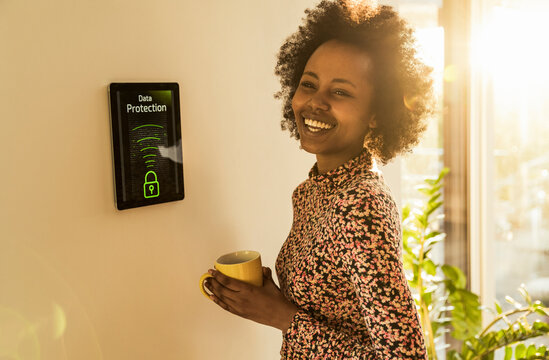 Cheerful woman with coffee cup standing by home automation device