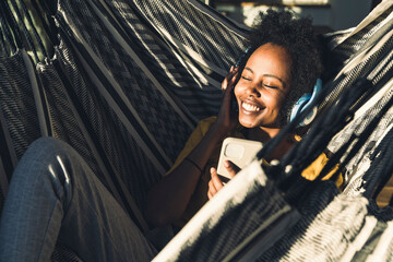 Smiling woman with headphones and mobile phone lying on hammock