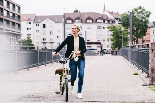 Mature businesswoman wheeling bicycle on bridge in city