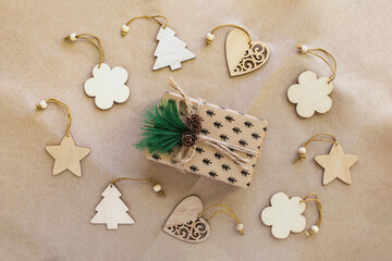 Christmas background from various wooden toys Christmas trees, hearts, flowers and stars around a festive gift in the center with a fir branch and cones, lie on brown craft paper, top view