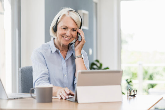 Saleswoman adjusting headset while working on digital tablet at home office