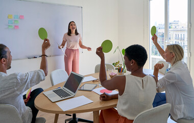 Cheerful businesswoman looking at coworkers holding paper for voting in meeting