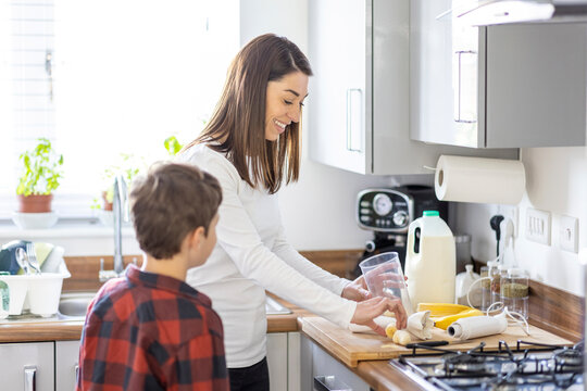 Smiling mother putting banana in jar by son in kitchen