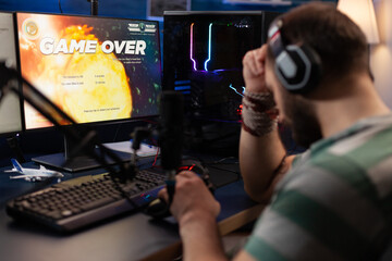 Adult playing video games on live stream with chat and losing. Man using headphones and microphone to broadcast gameplay, streaming lost game on computer. Gamer live streaming online.