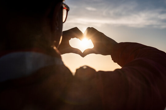 Woman making heart shape with hands during sunset