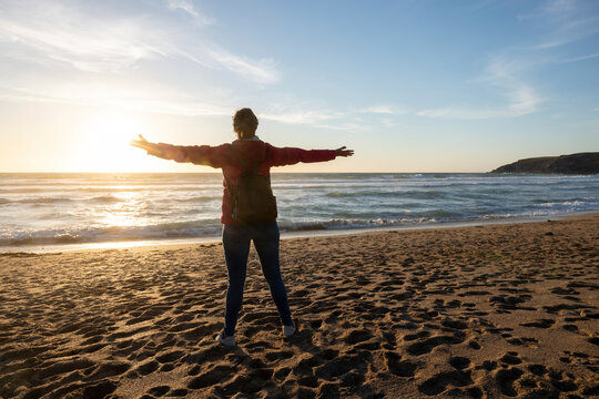 Woman standing with arms outstretched at beach during sunset