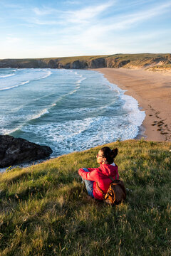 Woman with backpack sitting on grass near beach during sunset
