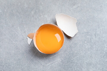 Cracked eggshell with raw yolk on light grey table, top view