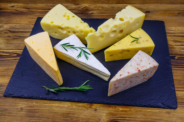 Set of various types of cheese on black slate board on a wooden table