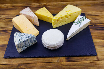 Set of various types of cheese on black slate board on a wooden table