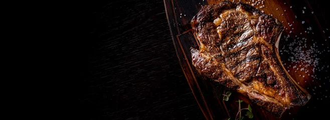 Poster Grilled Ribeye Steak on bones on wooden board, prime cowboy steak on dark background © pavel siamionov