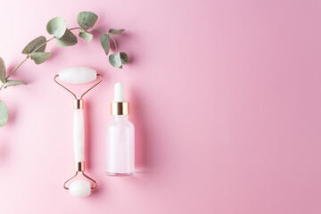 Composition of white mockup serum bottle, pink quartz stone face roller on pink background. Natural cosmetics concept. Creative cosmetics flat lay with copy space.