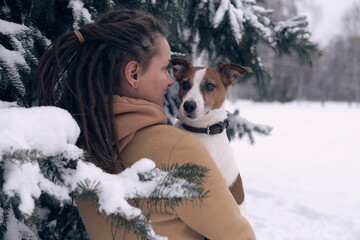 playful woman with dog. stylish hipster woman hugging and smiling cute puppy in snowy cold winter park. moments of true happiness.