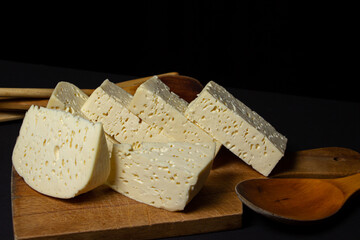 White cheese on a black background. Homemade white cheese on a wooden board. Traditional cuisine
